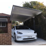 White car parked under a diy cantilever carport beside brick house.