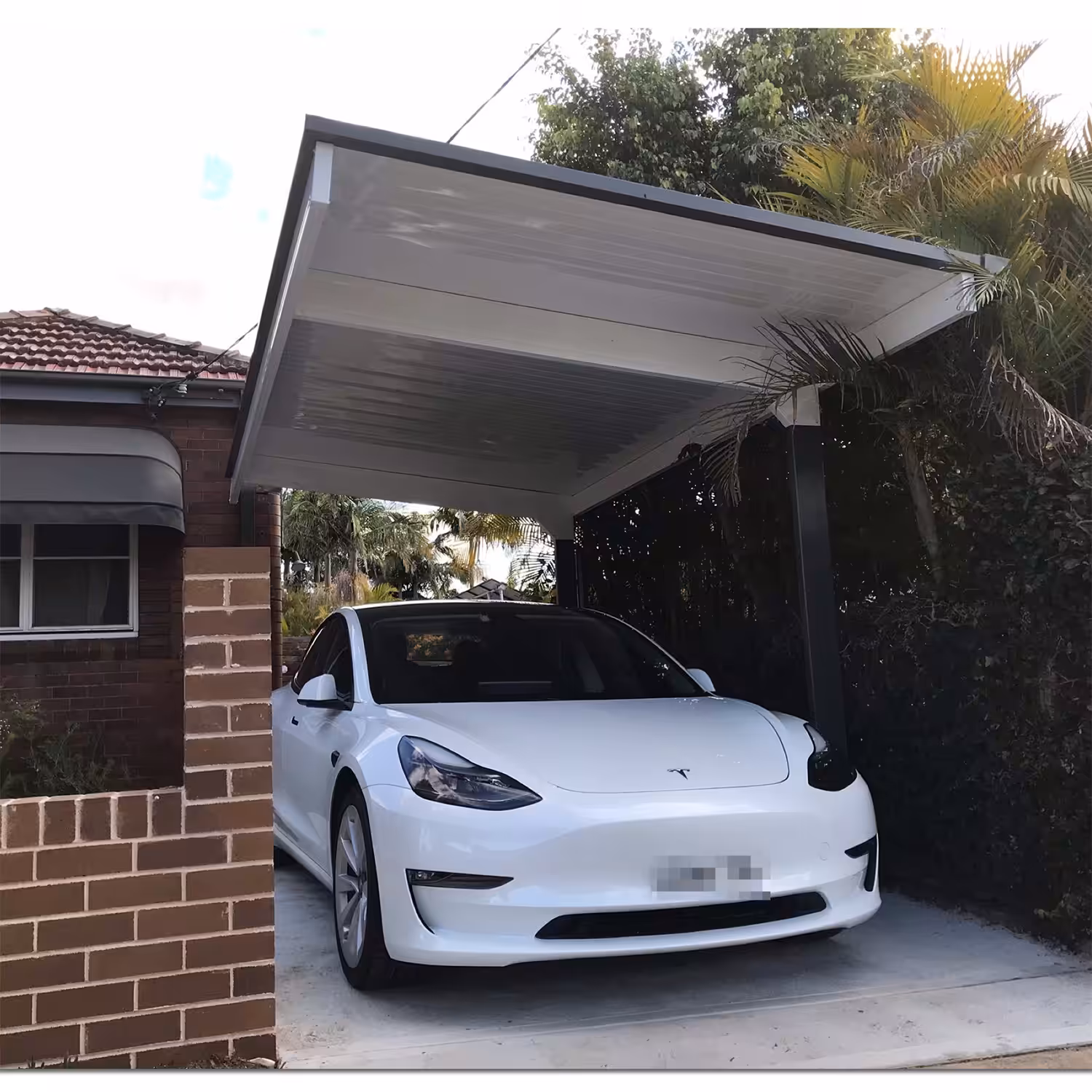 White car parked under a diy cantilever carport beside brick house.
