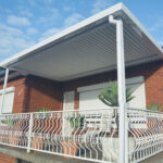 DIY attached flat roof pergola/patio of a brick house with plants.