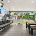 DIY attached flat roof pergola/patio with furniture and greenery.