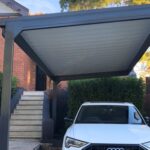 White car parked under diy cantilever carport beside a brick house.
