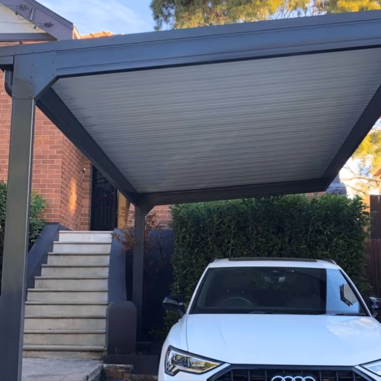 White car parked under diy cantilever carport beside a brick house.