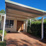 House entrance with DIY freestanding flat roof carport and brick path