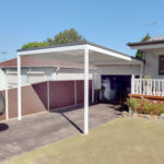 DIY attached flyover flat roof patio/pergola providing shade in residential backyard.