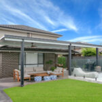 DIY attached flyover flat roof patio/pergola with green lawn and furniture.