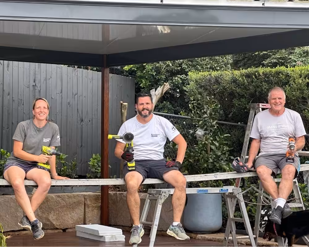 Three tradespeople seated with tools outdoors.